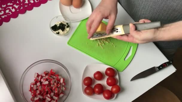 一个男人把磨碎的奶酪切碎 放在一个装有螃蟹棒的容器里 螃蟹棒 鸡蛋和西红柿的烹饪沙拉 — 图库视频影像