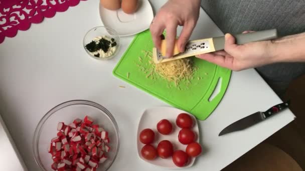A man chops grated cheese and puts it in a container with crab sticks. Cooking salad of crab sticks, cheese, eggs and tomatoes. — Stock Footage Man Chops Grated Cheese Puts Container Crab Sticks Cooking Salad Stock Video