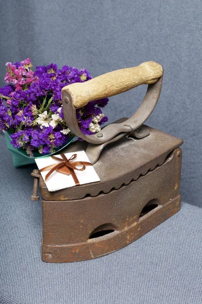 Old iron, heated by hot coals. Located on gray fabric. Nearby are bouquet of dried flowers and a greeting card.