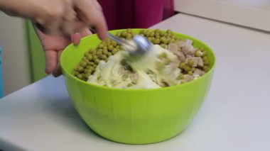 Bir kadın bir kap içinde bir salata karıştırma. Et salatası yumurta, patates, salatalık ve bezelye ile pişirme.