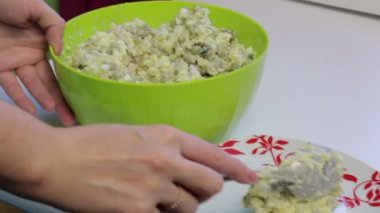 Bir kadın bir salata kapsayıcıdan bir tabağına koyuyor. Et salatası yumurta, patates, salatalık ve bezelye ile pişirme.