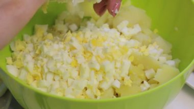 Kadın diğer malzemelerle bir kapta haşlanmış yumurta yendi. Et salatası yumurta, patates, salatalık ve bezelye ile pişirme.