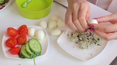 Bir kadın bıldırcın haşlanmış yumurta kabuk temizler. Bir kenara koyarak. Salata hazırlık için.
