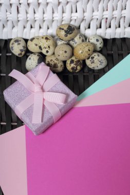 Bıldırcın yumurtası bir hasır asma yüzeyinde yalan. Kağıt ambalaj sarılı ve bir kurdele ile bağlanmış bir hediye kutusuyla diğerine. Adet arka plan için renkli kağıt.