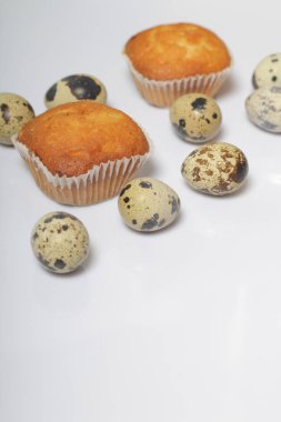 Bıldırcın yumurtası beyaz yüzeyinde yalan. Yakınlarda kekler bulunmaktadır.  