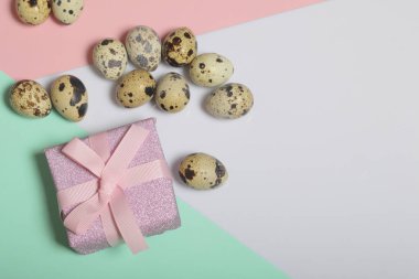 Bıldırcın yumurtası beyaz yüzeyinde yalan. Kağıt ambalaj sarılı ve bir kurdele ile bağlanmış bir hediye kutusuyla diğerine. Adet arka plan için renkli kağıt.