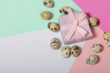 Bıldırcın yumurtası beyaz yüzeyinde yalan. Kağıt ambalaj sarılı ve bir kurdele ile bağlanmış bir hediye kutusuyla diğerine. Adet arka plan için renkli kağıt.