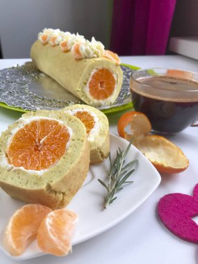 Bisküvi rulo pişirme ricotta ve mandarin ile doldurulmuş. Hazır rulo bir tepside yatıyor. Sonraki tabağı üzerinde rulo kesme parçasıdır.