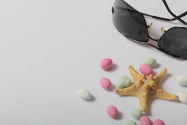 Summer holiday accessories. Sunglasses. Colored pebbles and starfish on a white background. clipart