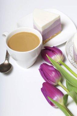 Yaban mersinli cheesecake. Bir uçan daire üzerinde hazır tatlı bir parça. Jöle katmanları farklı renklerde görülebilir. Bir fincan kahve ve bir buket Lale.