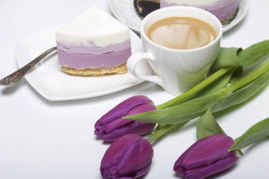 Yaban mersinli cheesecake. Bir uçan daire üzerinde hazır tatlı bir parça. Jöle katmanları farklı renklerde görülebilir. Bir fincan kahve ve bir buket Lale.