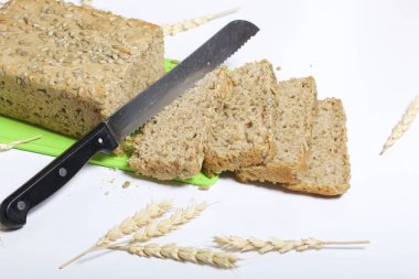 Evde ekmek. Bir somun taze pişmiş kepekli ekmek kesme tahtası üzerinde Ayçekirdeği yalanlarla. Ekmek dilimleri ve bir bıçak görülebilir.