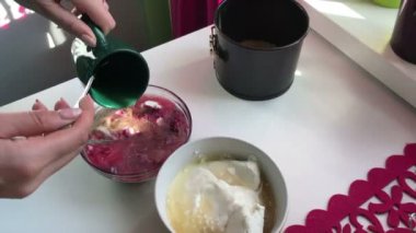 Kadın çözünmüş jelatin süzme peynir için ekler. Yaban mersinli cheesecake. Yemek pişirmek için malzemeler tablo yüzeyinde yer alır.