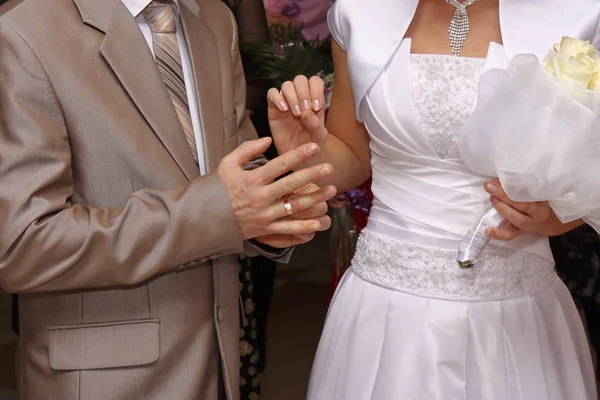 Der Bräutigam im Hochzeitsanzug legt der Braut einen Ehering an. sie hält einen Hochzeitsstrauß in einer anderen Hand. — Stockfoto