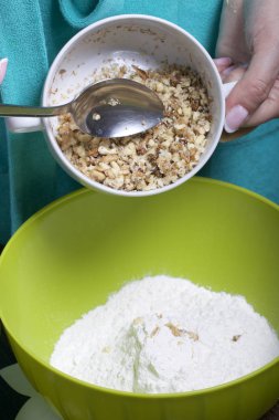 Kadın ceviz ekler. Pasta Bisküvi kırıntıları ve süt jöle yemek. Tablo yüzeyinde malzemeler ve mutfak aletleri vardır.