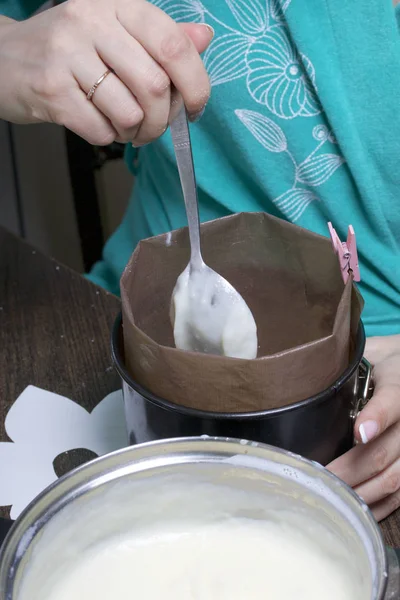 Woman adds milk jelly to cake mold. Cooking a cake of biscuit crumbs and milk jelly. On the surface of the table are the ingredients and cooking utensils.