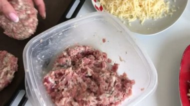 Bir kadın kıyma köftesi sculpts ve onları fırın tepsisine bırakır. Kıyma biftek patates, yumurta ve peynir ile. Pişirme adımları ve malzemeler.