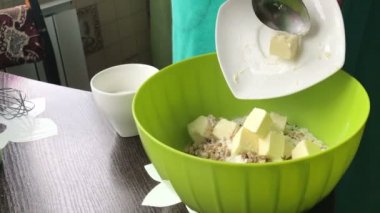 Kadın yemek için tereyağı ve şeker ekleyin. Pasta Bisküvi kırıntıları ve süt jöle yemek. Tablo yüzeyinde malzemeler ve mutfak aletleri vardır.