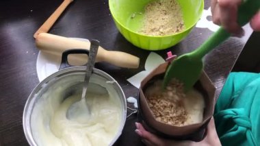 Kadın pandispanya kek kalıp için ekler. Pasta Bisküvi kırıntıları ve süt jöle yemek. Tablo yüzeyinde malzemeler ve mutfak aletleri vardır.