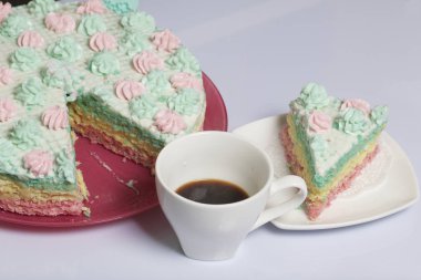 Parça kesilir ve bir daire üzerinde yan yana yatıyor. Yakınlarda bir fincan kahve var. Krem yapılan gözleme pasta kek batırılmış. Krem çiçeklerle süslenmiş.