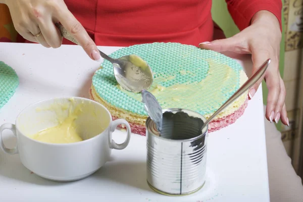 A woman lubricates the cakes and puts in a pile. Round wafer cakes of different colors. For making waffle cake. Nearby there is a can of condensed milk to soak the cakes.