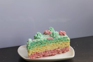 Parça kesilir ve bir daire üzerinde yan yana yatıyor. Krem yapılan gözleme pasta kek batırılmış. Krem çiçeklerle süslenmiş.