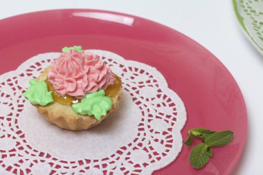 Sepet kek farklı renkteki krema ile dekore edilmiştir. Reçel doldurma. Nane yaprakları ile süslenmiş.