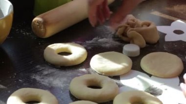 Bir kadın için Amerikan donut boşluklar yapıyor. Hamur yapılmış, tablo yüzeyinde yalan. Yakınlarda yemek pişirmek için araçlar bulunmaktadır.