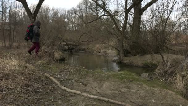 一名身穿头套的夹克男子在沿河的春园散步 成为泡沫 走得更远 春天风景 — 图库视频影像
