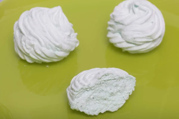 Domácí marshmallows kladen na talíři. Proutěná s mátou, se zeleným nádechem. Nedaleko je kus marshmallow, jeho řezu je vidět. Na světle zeleném pozadí. — Stock fotografie