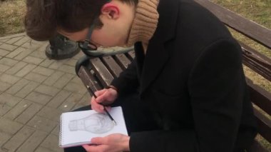 Genç bir adam bir bankta oturur ve bir defterde skeçler yapar. Bahar, havalı hava, adam siyah bir ceket giyiyor. Retro tarzında rahat avlu