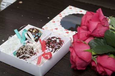 Pasta çıkar güzel bir hediye kutusunda paketlenmiştir. Yakınlarda bir saydam pencere ve bir buket kırmızı gül ile bir kapak var. Karanlık bir arka plan üzerinde.