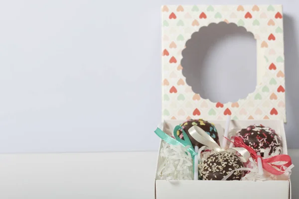Cake pops are beautifully packed in a gift box. Nearby there is a cover with a transparent window. On a white background.