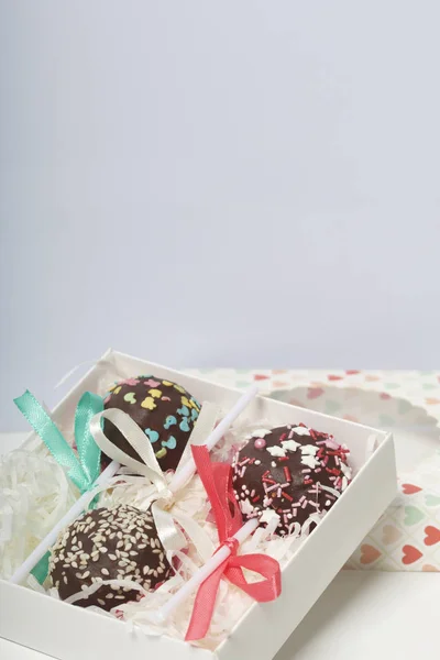 Cake pops are beautifully packed in a gift box. Nearby there is a cover with a transparent window. On a white background.