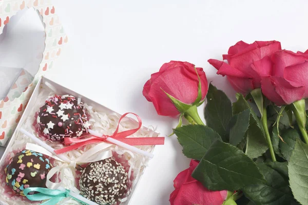 Los pastelitos están bellamente empaquetados en una caja de regalo. Cerca hay una cubierta con una ventana transparente y un ramo de rosas escarlata . — Foto de Stock