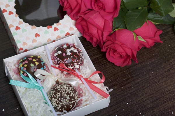 Пирожные палочки красиво упакованы в подарочную коробку. Рядом находится крышка с прозрачным окном и букет алых роз. На темном фоне . — стоковое фото