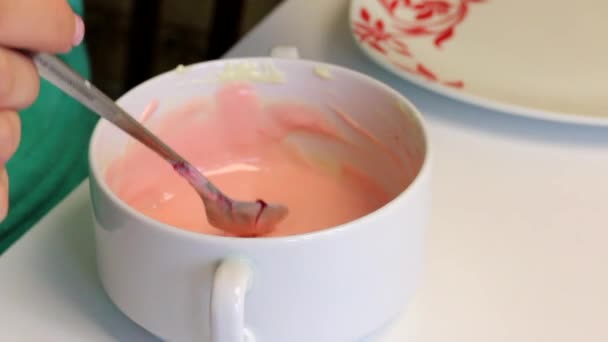 一个女人在融化的白巧克力上加了一滴食物着色 并将其混合 蛋糕泡的烹饪釉面 — 图库视频影像