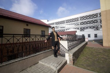 Ayakta, eski kentsel binalar arasında duran bir gülümseme pozlar olan genç bir adam. Bir siyah ışık Mont, siyah çerçeveli gözlük giyinmiş.