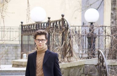 Genç bir adam bir gülümseme ile eski şehir'in mimaride öğeleri arasında teşkil etmektedir. Bir siyah ışık Mont, siyah çerçeveli gözlük giyinmiş.