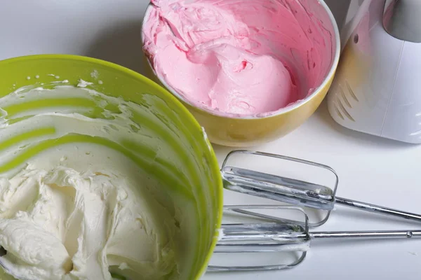 Panna montata di diversi colori. Nelle vicinanze si trovano i battitori e il frullatore. Crema per decorare la torta con strati di diversi colori . — Foto Stock