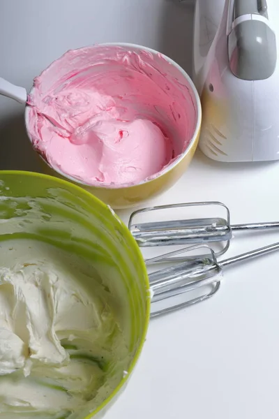 Panna montata di diversi colori. Nelle vicinanze si trovano i battitori e il frullatore. Crema per decorare la torta con strati di diversi colori . — Foto Stock