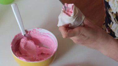 Bir kadın bir pembe krema pasta torbaya koyar. Sonraki sünger kek ile beyaz krema spread.