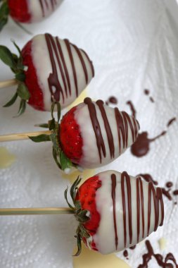 Siyah ve beyaz çikolatada sırlı çilek bir plaka üzerinde kurur. Çalışma yüzeyi çikolata görünür damla üzerinde. Çikolatada sırlı pişirme çilek.