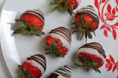 Siyah ve beyaz çikolatada sırlı çilek. Bir desen ile beyaz bir plaka üzerinde yalan.