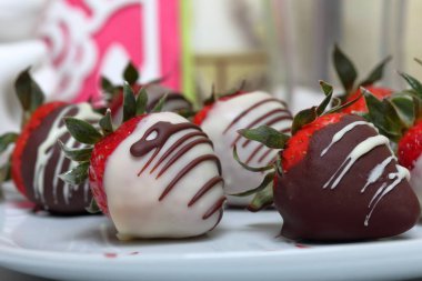 Siyah ve beyaz çikolatada sırlı çilek. Bir desen ile beyaz bir plaka üzerinde yalan.