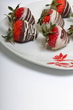 Siyah ve beyaz çikolatada sırlı çilek. Bir desen ile beyaz bir plaka üzerinde yalan.