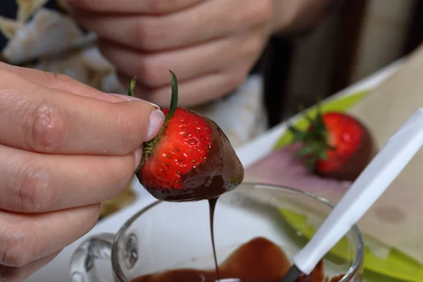 女性が黒の溶かしたチョコレートでイチゴをディップします。イチゴをチョコレートに釉薬をかけて調理. — ストック写真