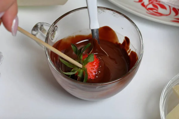 女性が黒の溶かしたチョコレートでイチゴをディップします。イチゴをチョコレートに釉薬をかけて調理. — ストック写真