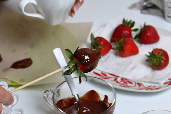 女性が黒の溶かしたチョコレートでイチゴをディップします。イチゴをチョコレートに釉薬をかけて調理. — ストック写真