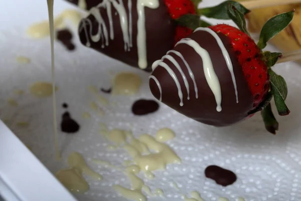 Jordgubbar glaserade i svart och vit choklad torkar på en tallrik. På arbets ytan synliga droppar av choklad. Matlagning jordgubbar glaserade i choklad. — Stockfoto